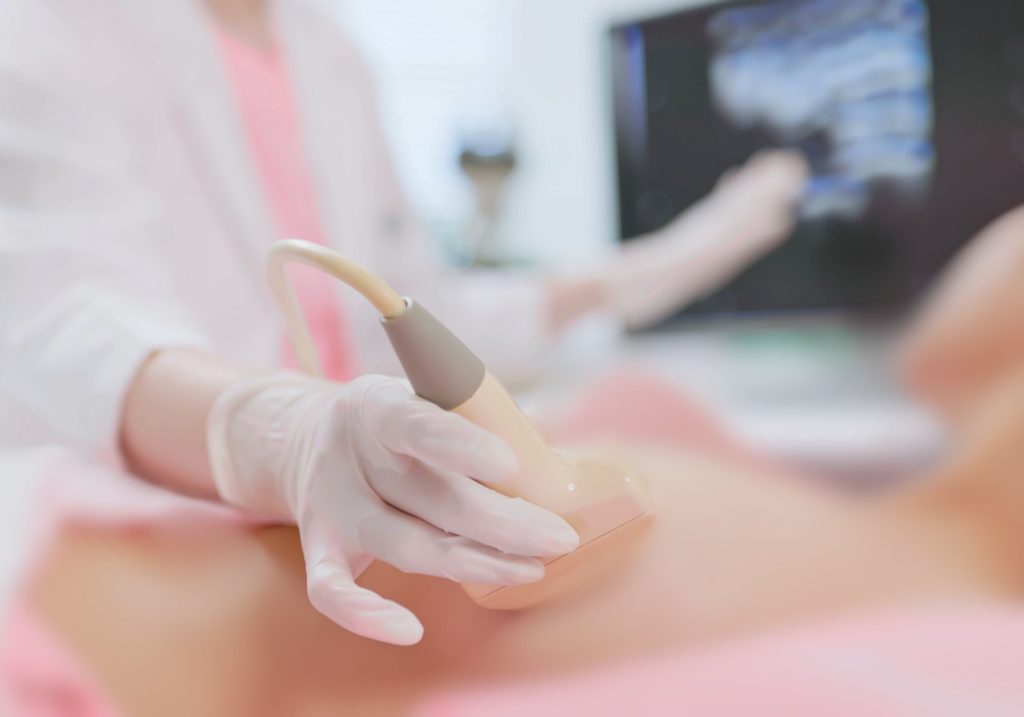 Lekarz w rękawiczkach lekarskich przykłada głowicę USG do piersi Pacjentki - ilustracja dotycząca USG piersi w Centrum Medycznym neoMedica w Poznaniu.