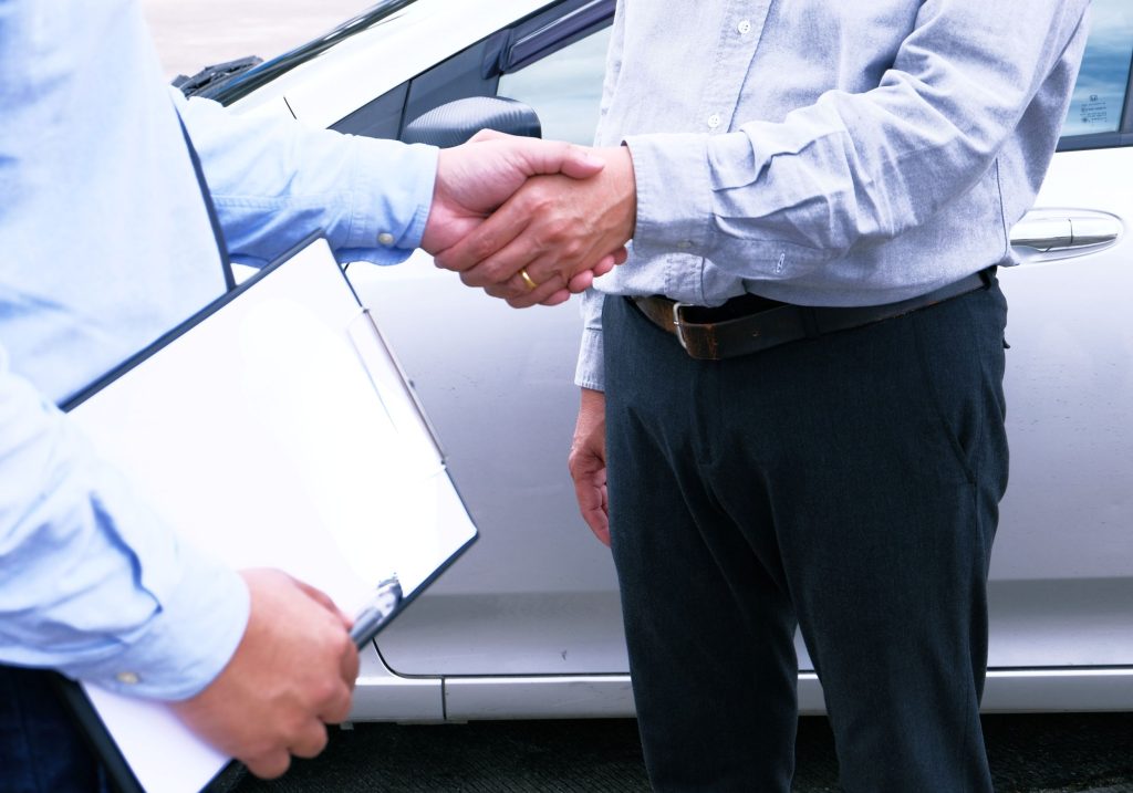 Dwóch mężczyzn podający sobie dłóń, w tle samochód - ilustracja dotycząca badań kierowców w Centrum Medycznym neoMedica w Poznaniu.